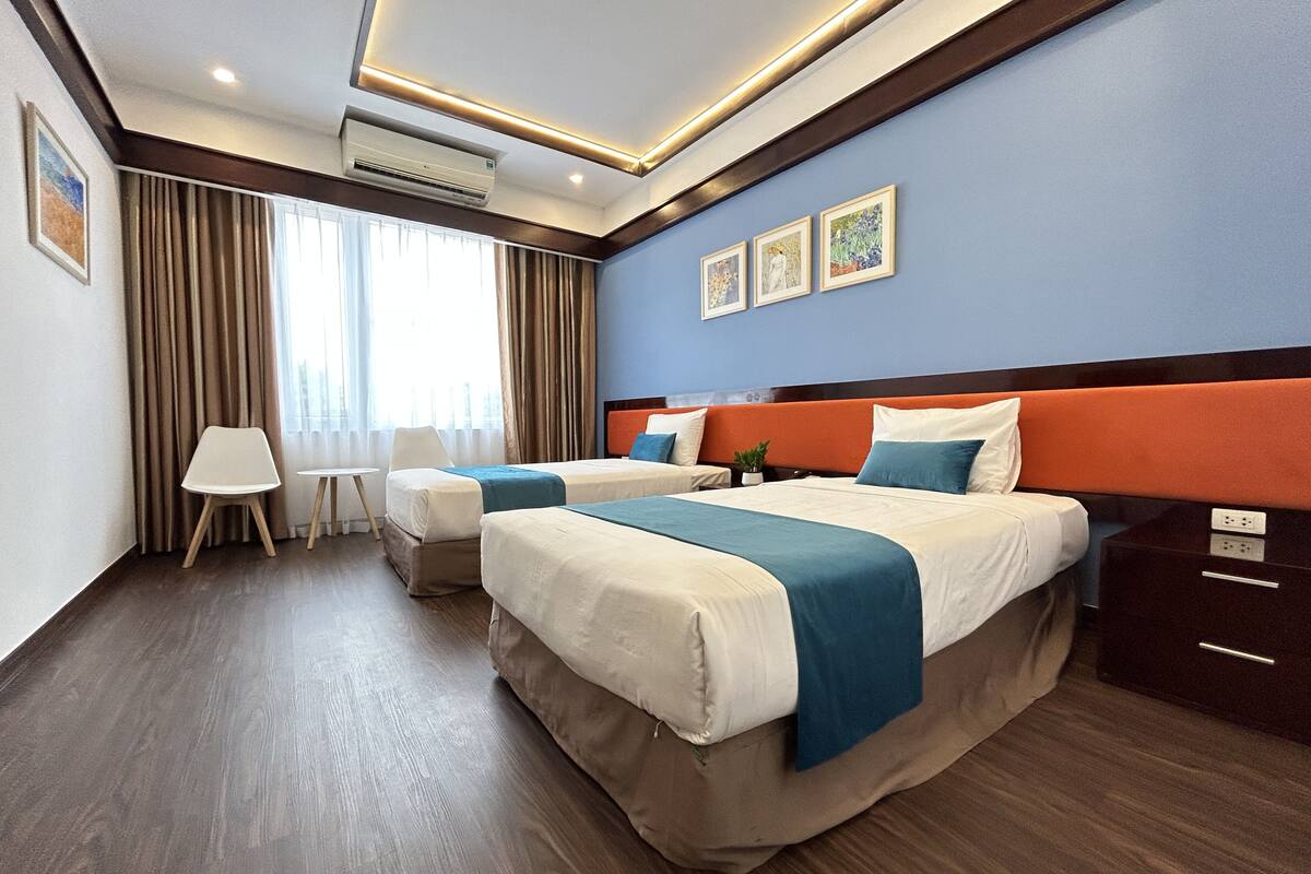 A hotel room with two beds, a desk, a chair, and a window with curtains.