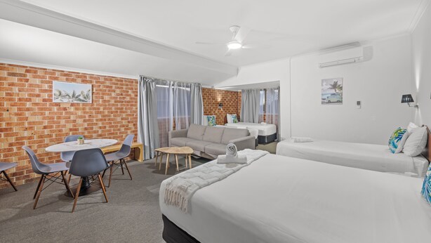 Une chambre d’hôtel avec un mur en briques, une table de salle à manger ronde entourée de chaises, un canapé, un lit et une petite table avec une lampe.