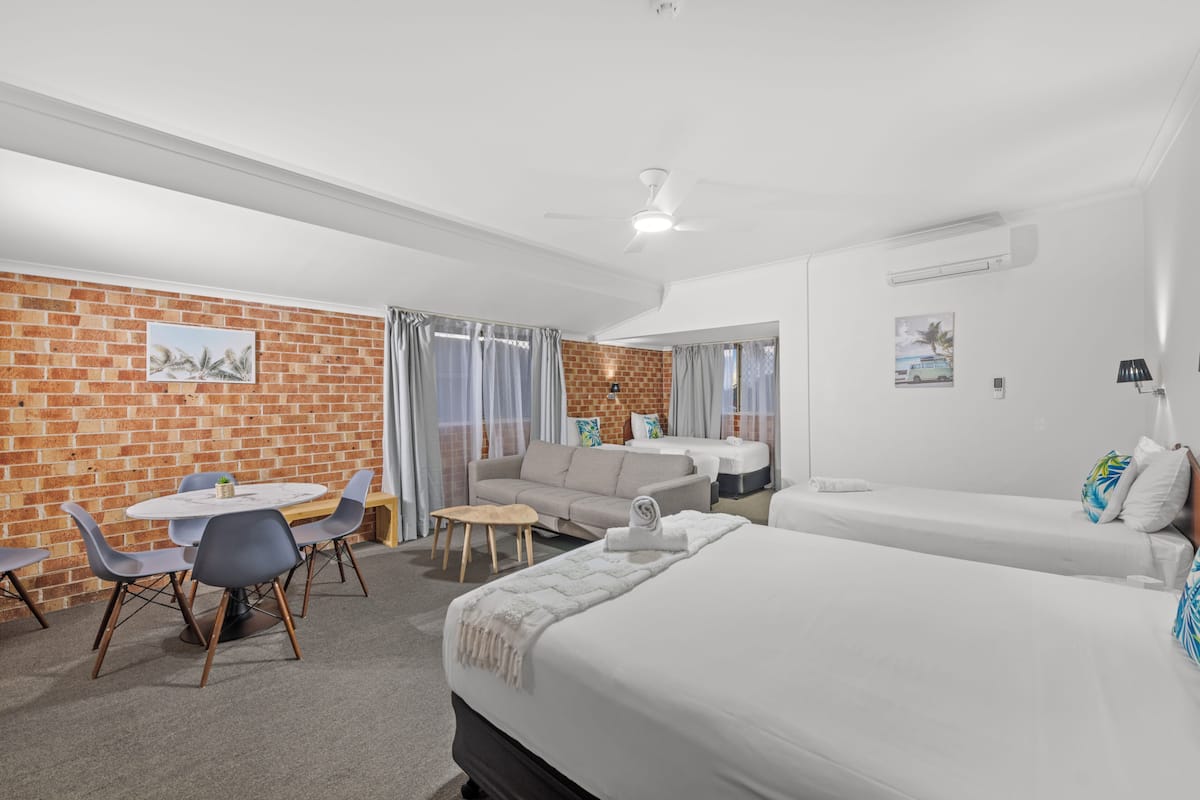 Een hotelkamer met een bakstenen muur, een ronde eettafel met stoelen, een bank, een bed en een kleine tafel met een lamp.