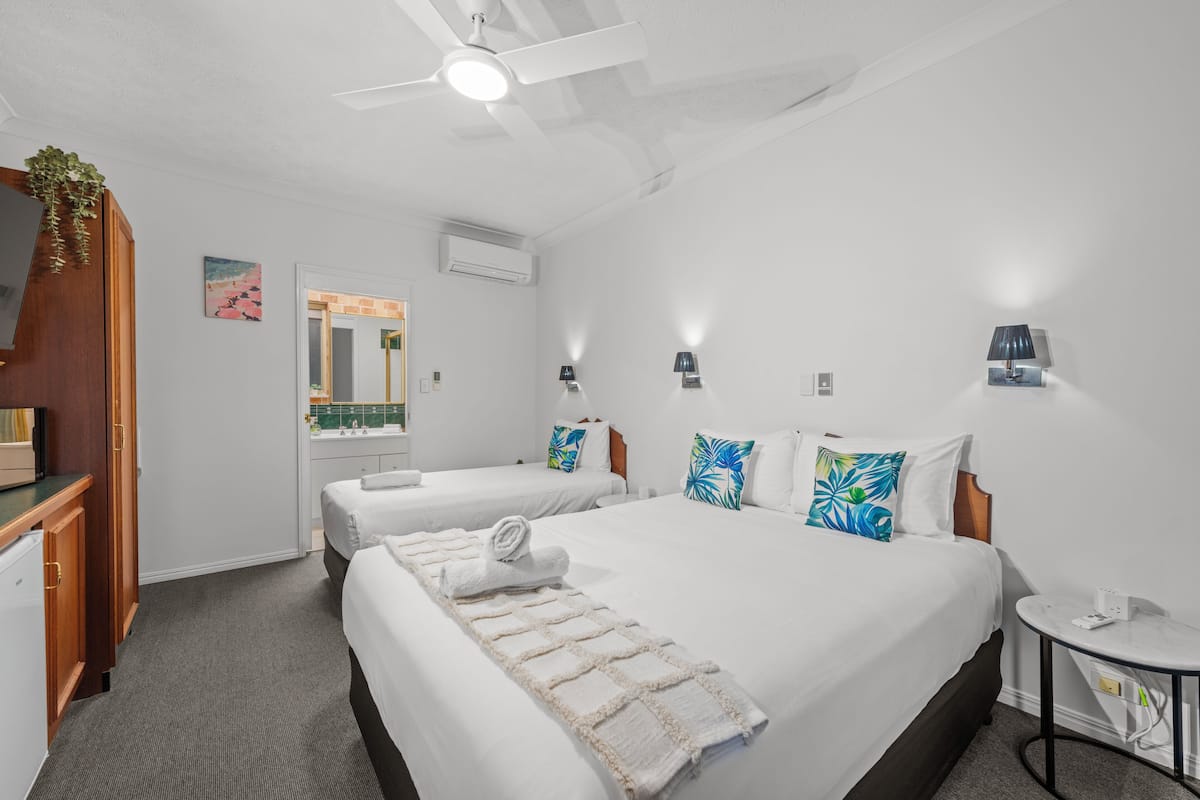 Een hotelkamer met twee bedden, een plafondventilator, een klein rond tafeltje en een wandairconditioner.