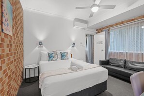 Une chambre d’hôtel avec un lit, un canapé, une petite table et un ventilateur de plafond.