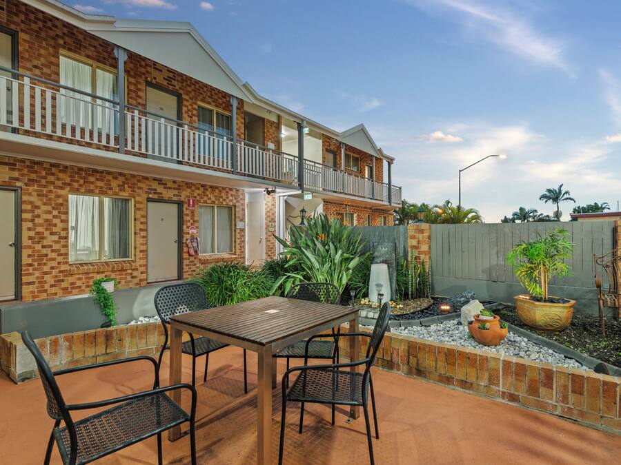 A two-story building with a balcony, outdoor seating area with a table and chairs, and potted plants.