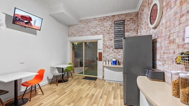 Een moderne keuken met een koelkast, een eethoek met stoelen en een aan de muur bevestigde televisie.