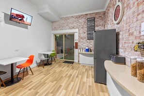 A modern kitchen with a refrigerator, a dining area with chairs, and a TV mounted on the wall. - Airport Clayfield Motel (Clayfield)