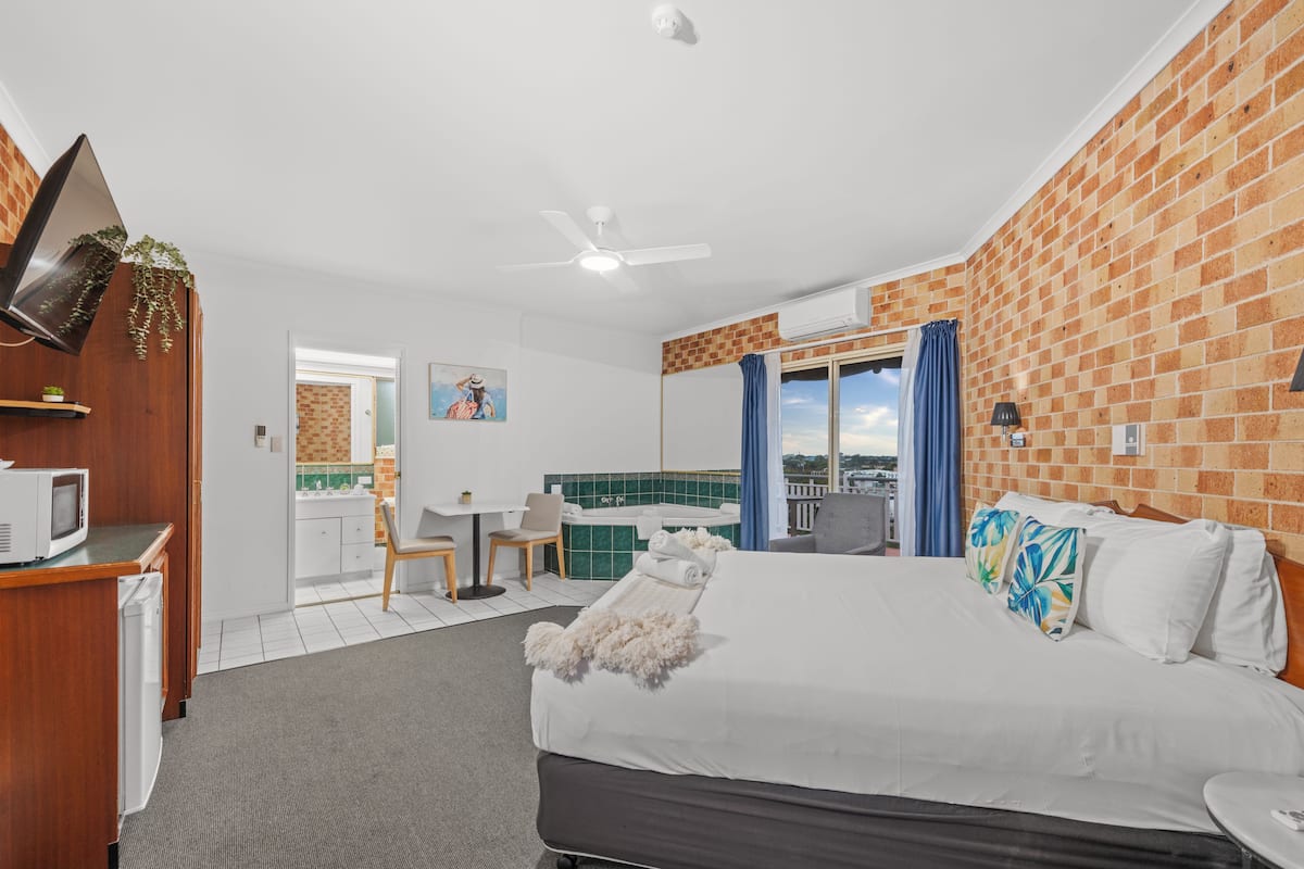 Hotelkamer met een bed, bureau, televisie, een kleine kitchenette en een balkon met uitzicht.