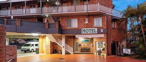 Un motel de dos pisos, con balcón y un letrero que indica los horarios de la piscina.