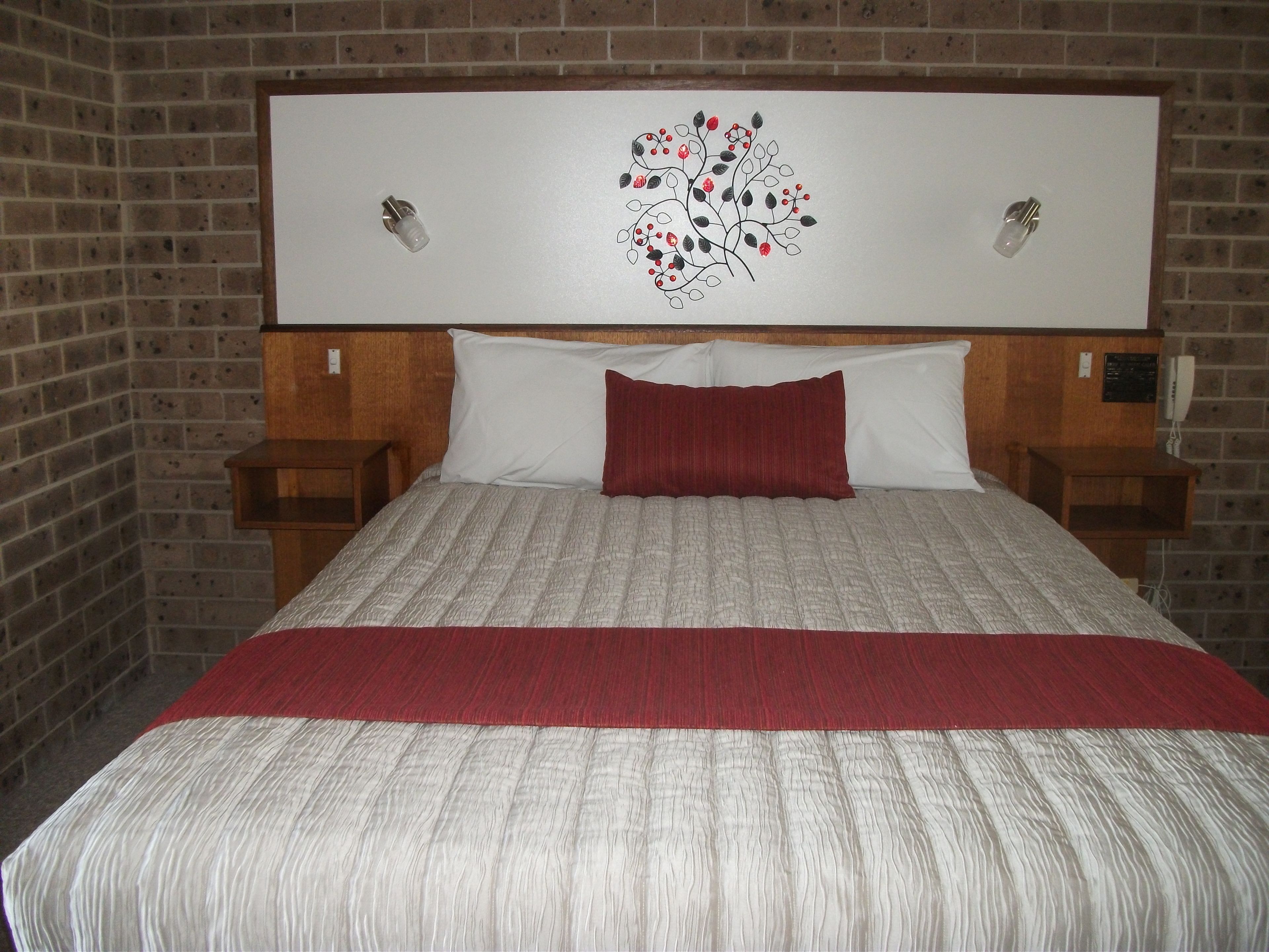 Una habitación de hotel con pared de ladrillo, una cama grande con cubrecama rojo y blanco, dos mesitas de noche y una obra de arte colgada en la pared.