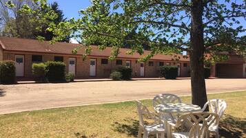 A motel with multiple rooms, a covered outdoor seating area, and a tree providing shade.