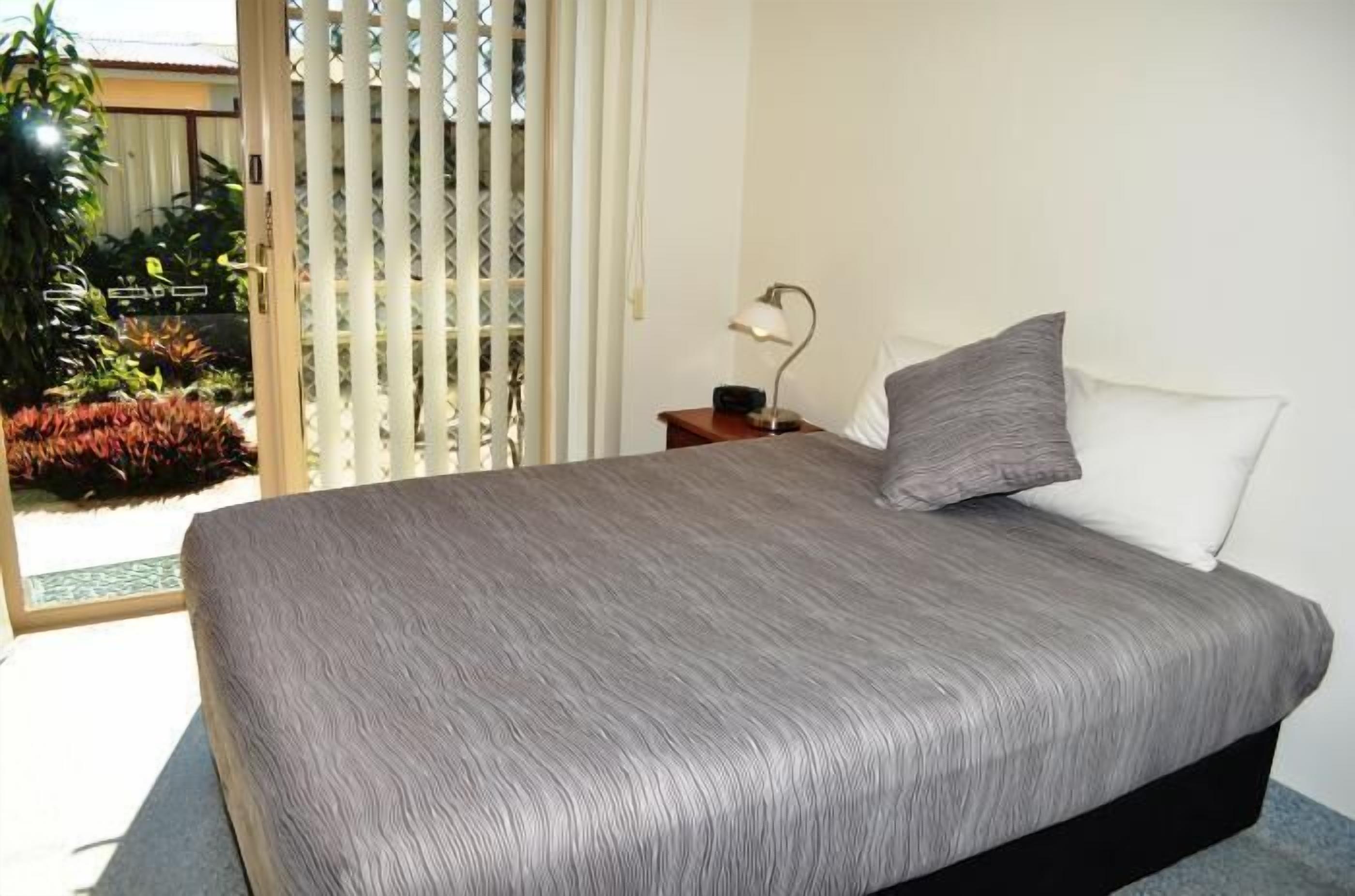Une chambre à coucher avec un lit, une table de chevet, une lampe et une vue sur un jardin, accessible par une porte coulissante.