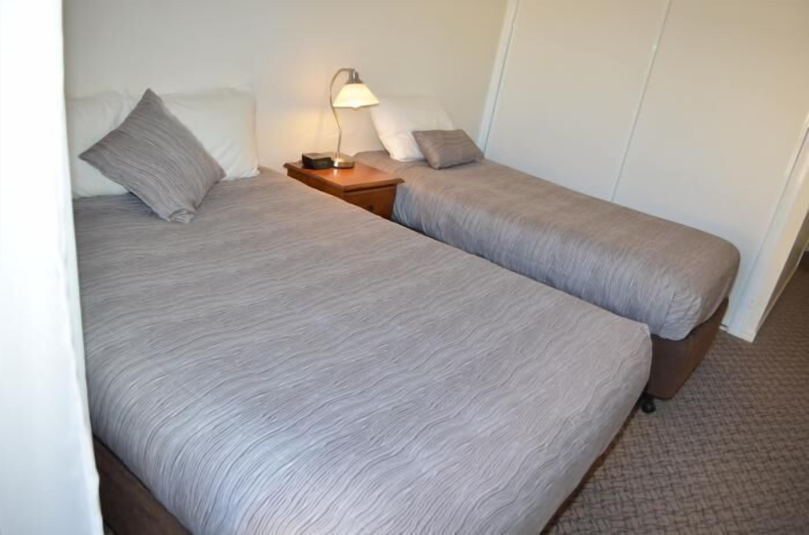 Une chambre avec deux lits, chacun étant équipé d’un oreiller et d’une table de chevet avec une lampe.