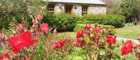Un edificio de piedra con techo inclinado y un jardín bien cuidado con flores rojas.