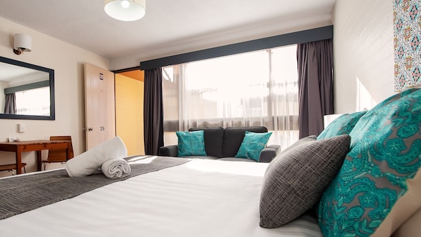 A hotel room with a bed, a desk, a chair, and a large window. - Albury Winsor Park Motor Inn (Albury)