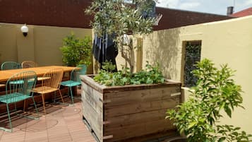 A patio with a wooden table and chairs, a raised garden bed, and a potted plant.