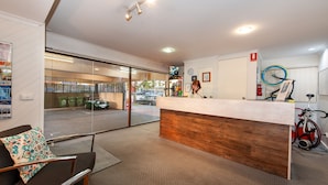 A reception area with a wooden reception desk, a seating area with a patterned pillow, and a bicycle mounted on the wall. - Albury Winsor Park Motor Inn (Albury)
