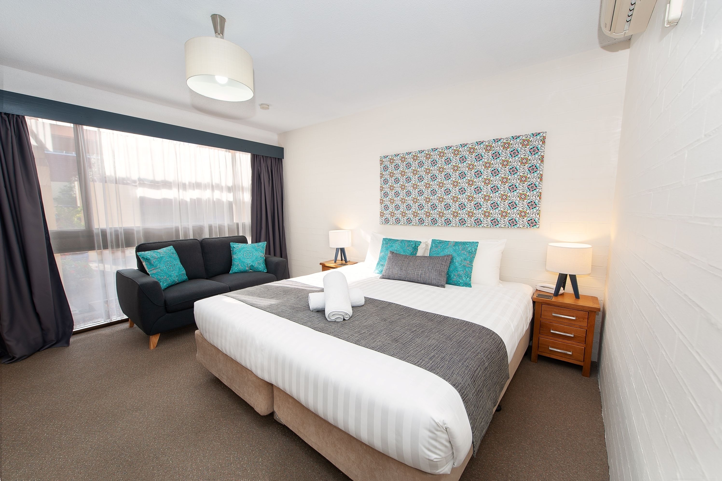 A hotel room with a large bed, a sofa, a nightstand, and a window with curtains.