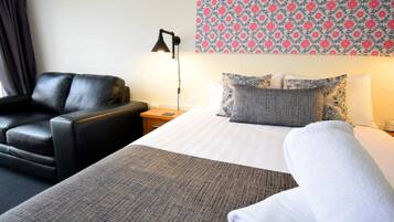 A hotel room with a bed, a chair, a bedside table, a lamp, and patterned wallpaper.