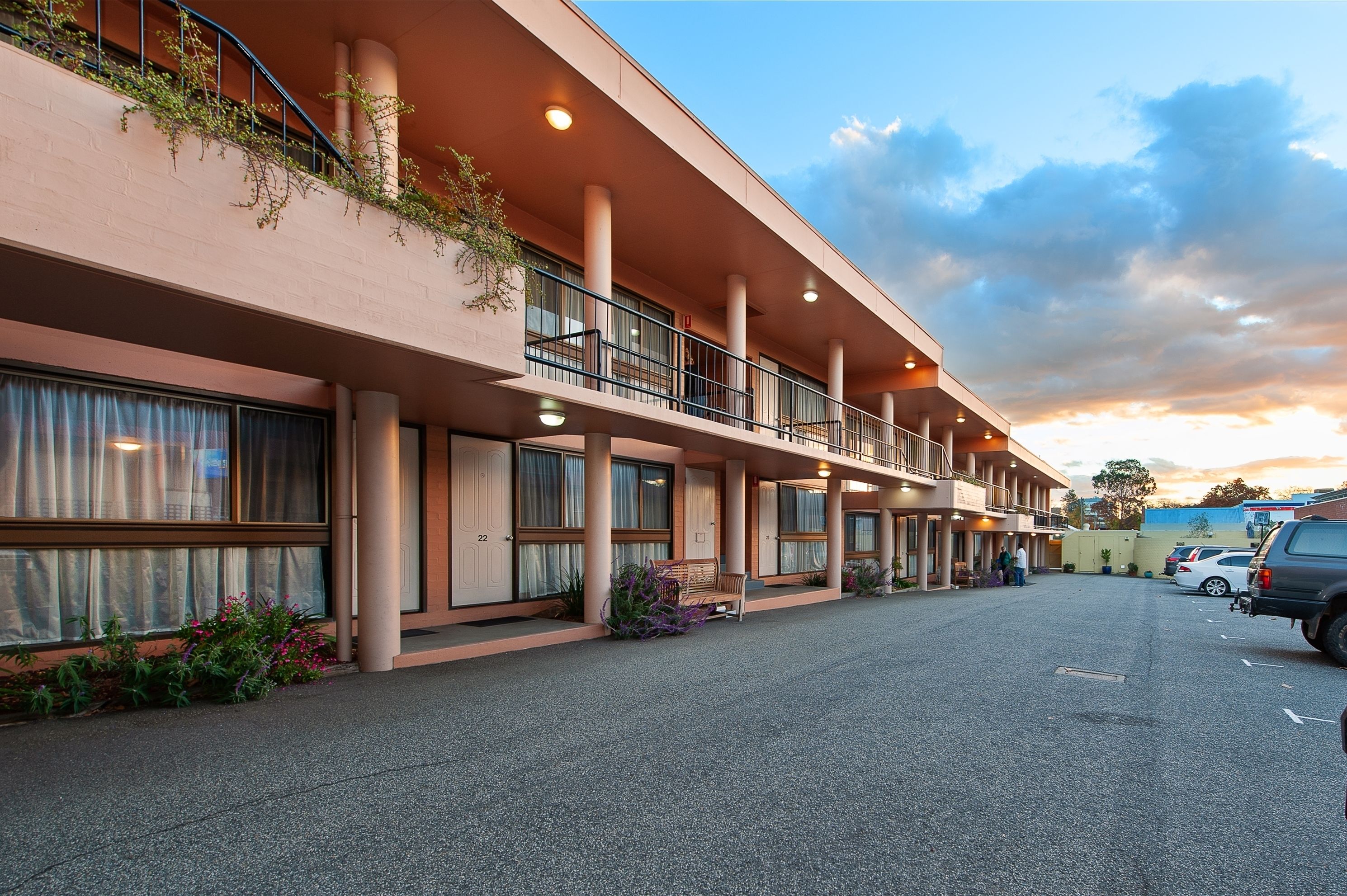 A hotel with a flat facade, multiple balconies, and a parking area.