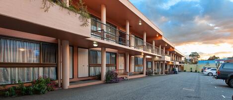 A hotel with a flat facade, multiple balconies, and a parking area.