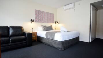 A hotel room with a bed, a black leather chair, a nightstand, two bedside lamps, and a patterned wall hanging.