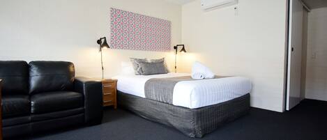 A hotel room with a bed, a black leather chair, a nightstand, two bedside lamps, and a patterned wall hanging.