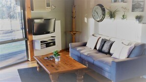 A living room with a grey sofa, a wooden coffee table, a flat-screen TV, and a clock on the wall.