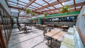 Un amplio patio interior con mesas y sillas de madera, plantas colgantes y suelo estampado.