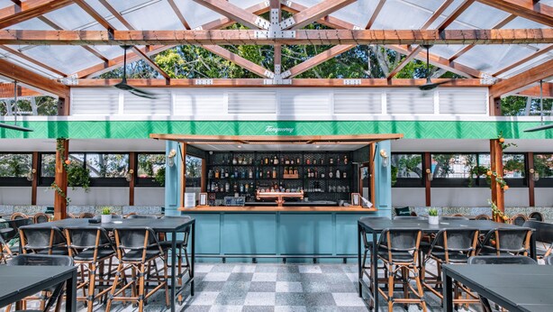 Zona de bar al aire libre con suelo a cuadros, sillas de madera y una barra que exhibe diferentes botellas.