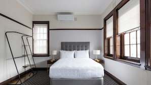 Un dormitorio ordenado con una cama grande, lámparas de noche, una ventana con persianas y un radiador.