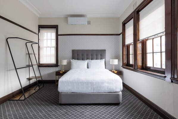 Quarto bem arrumado com uma cama grande, abajures, janela com persianas e radiador.