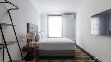 A hotel room with a bed, bedside table, lamp, and a TV mounted on the wall.
