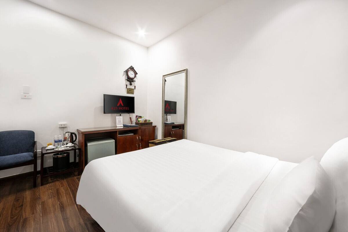 A hotel room with a bed, a desk with a computer, a chair, a television, and a clock on the wall.
