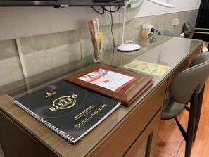 A hotel reception desk with a glass partition, a brown leather-bound book, a white desk lamp, and a chair. - A25 Hotel - 12 Lien Tri (Hanoi)