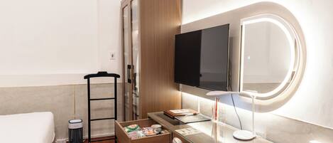 A hotel room with a bed, a desk with a computer, a TV, a mirror, and a wardrobe.