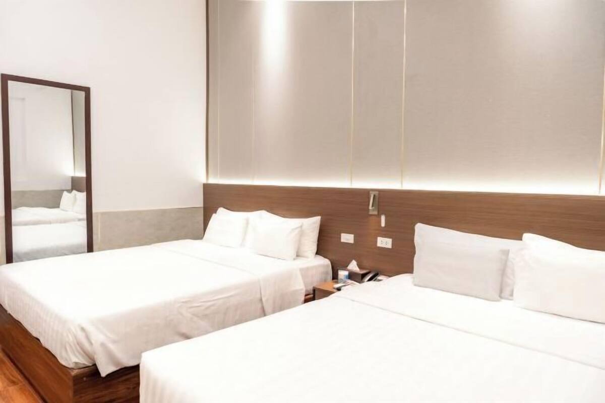 A hotel room with two beds, a wooden headboard, a mirror, and a bedside table with a lamp.