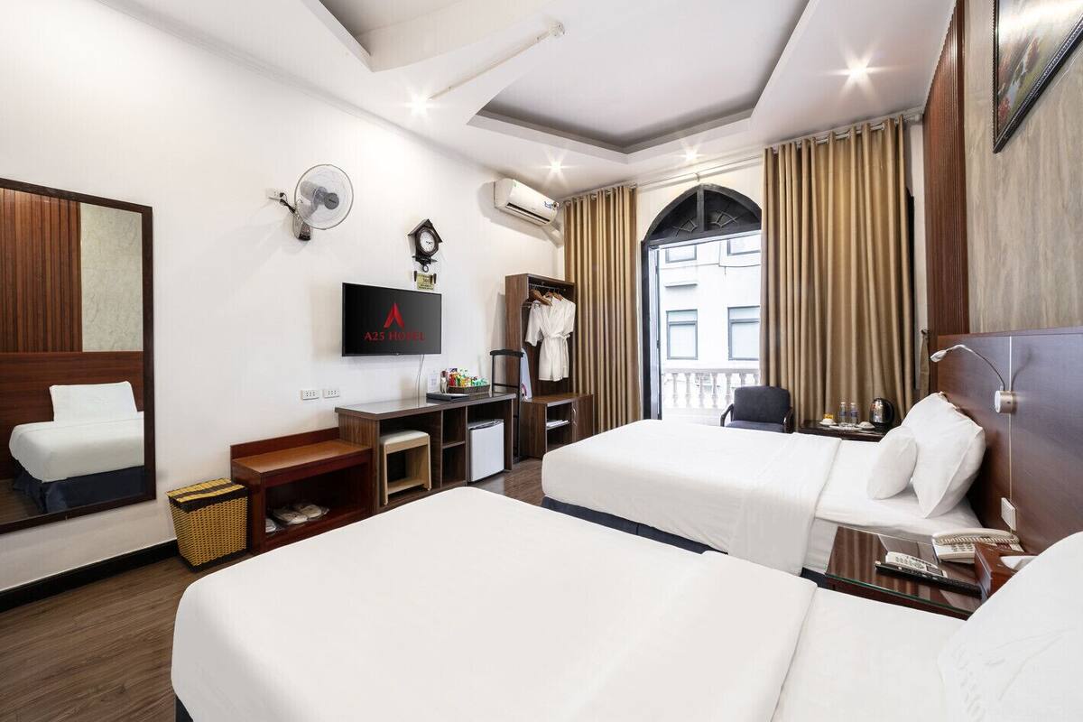 A hotel room with two beds, a TV, a desk, a wardrobe, and a view of the city.