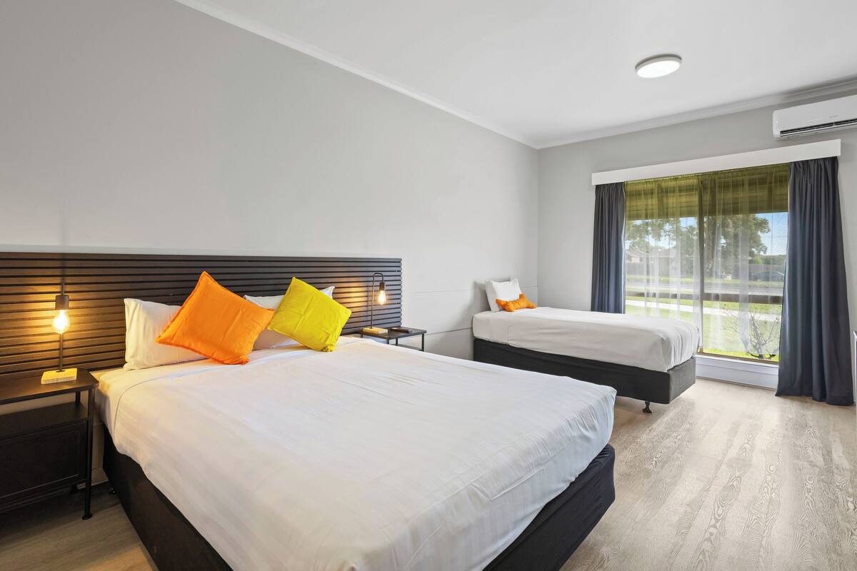 Une chambre d’hôtel avec deux lits, une fenêtre avec des rideaux, un luminaire au plafond et un appareil de climatisation.