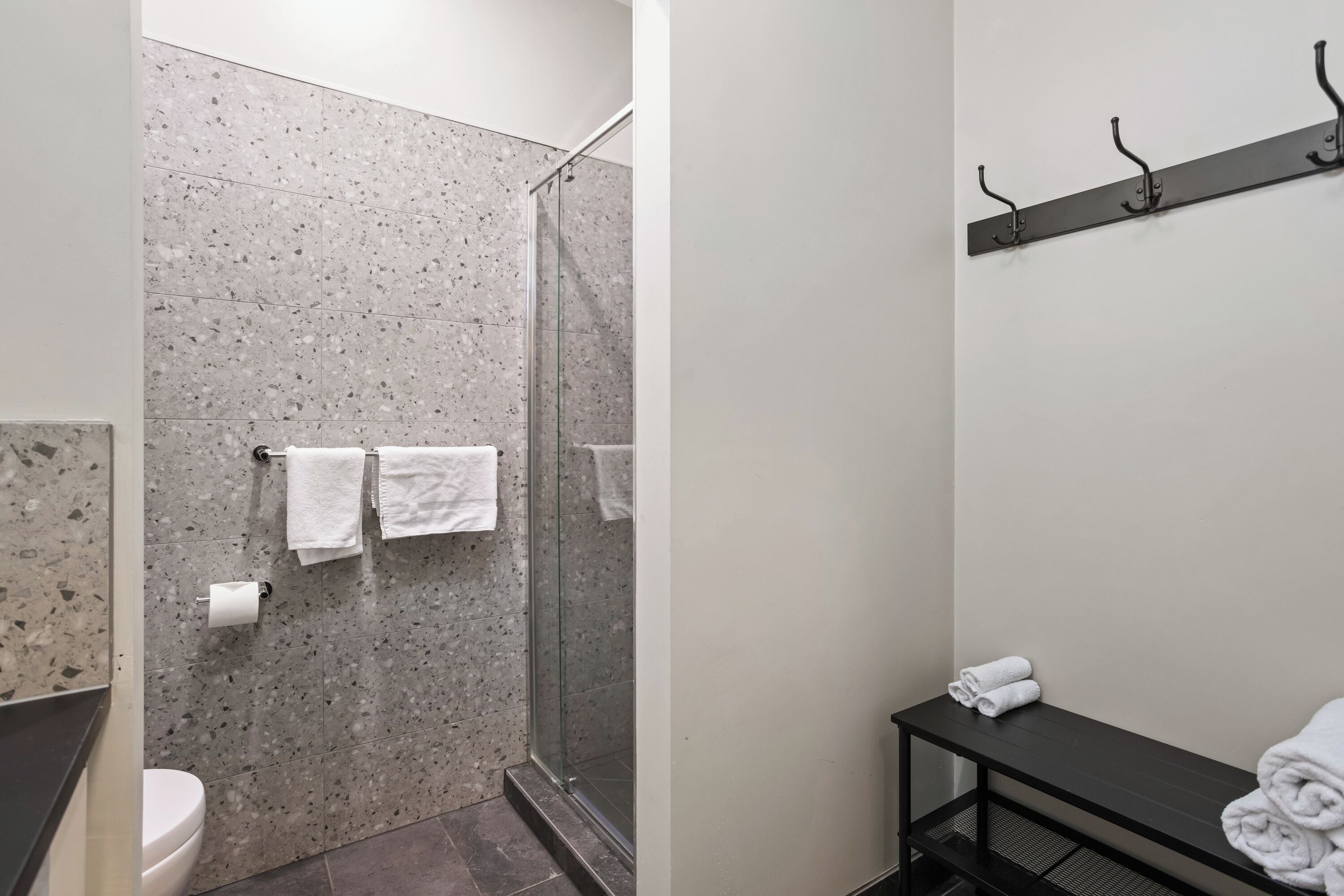 A bathroom with a shower, toilet, and a towel rack with towels.