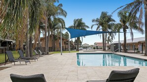 A swimming pool with lounge chairs, palm trees, and a blue shade sail. - Carrum Downs Motel (Carrum Downs)