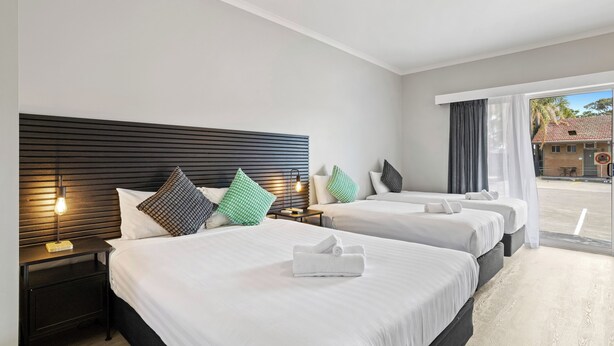 A hotel room with two beds, a nightstand with a lamp, and a view of the outside. - Carrum Downs Motel (Carrum Downs)
