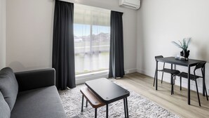 A modern living room with a sofa, a small table, and a dining area with chairs. - Carrum Downs Motel (Carrum Downs)