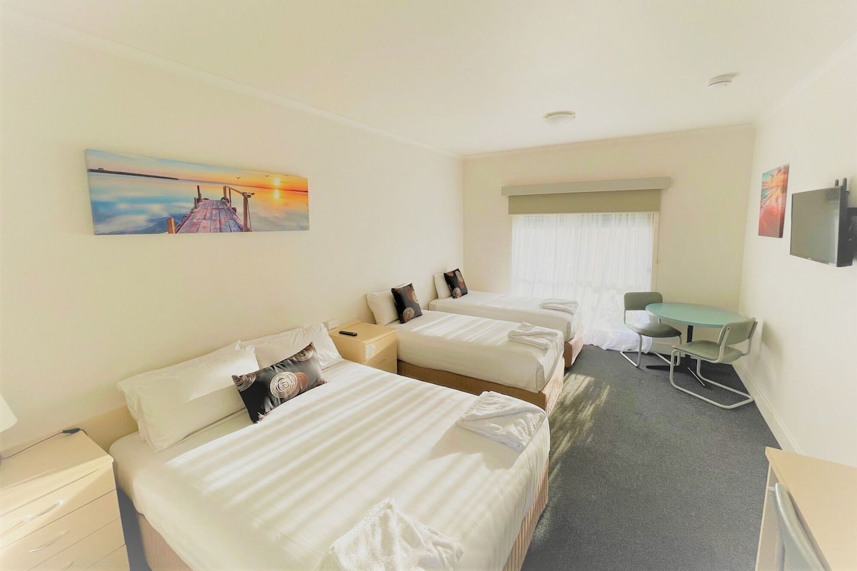 Una habitación de hotel con dos camas, un escritorio, una silla, un televisor y un cuadro en la pared.