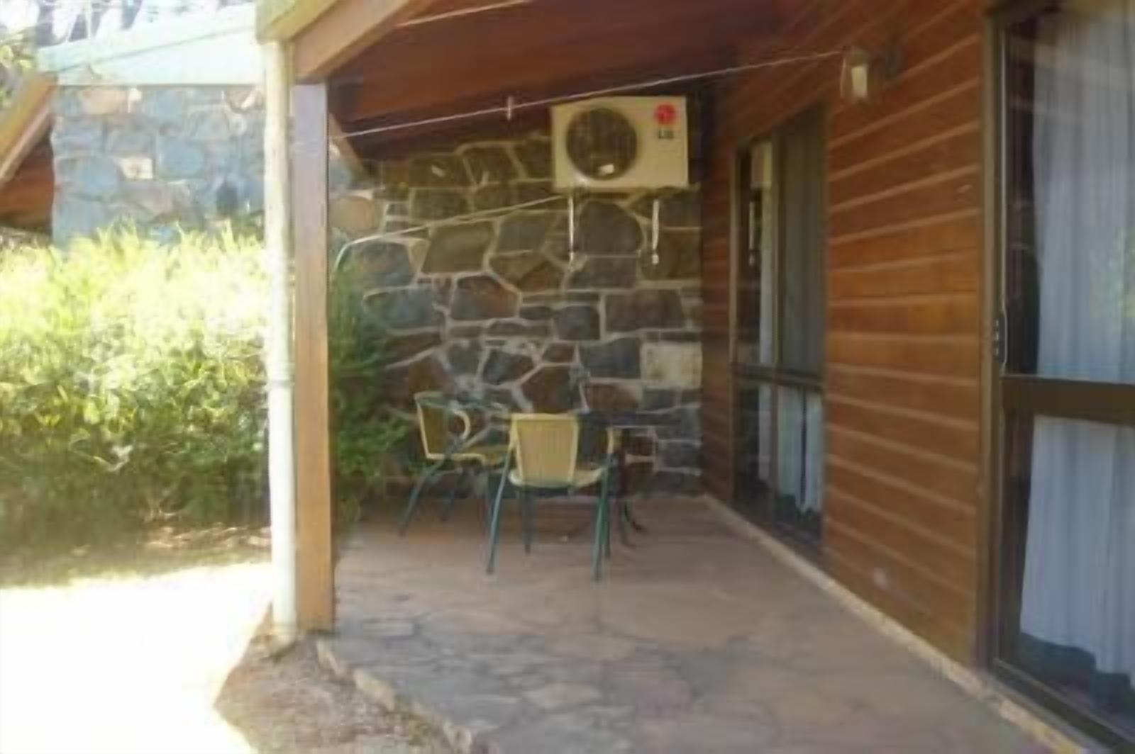 A covered outdoor area with a stone wall, a table with chairs, and a window with curtains.