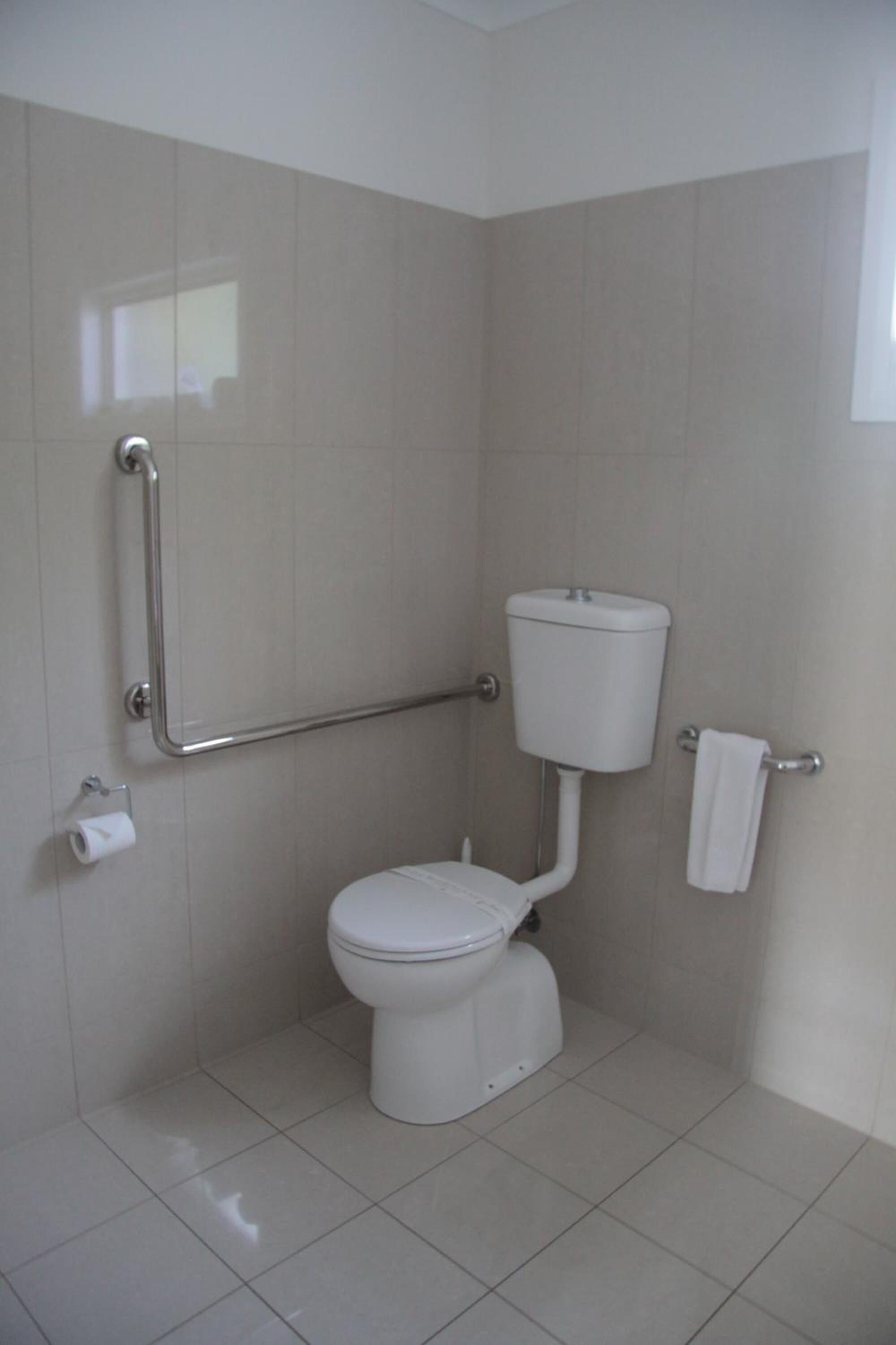 Un baño pequeño y moderno con inodoro blanco, barras de apoyo y un perchero para toallas.