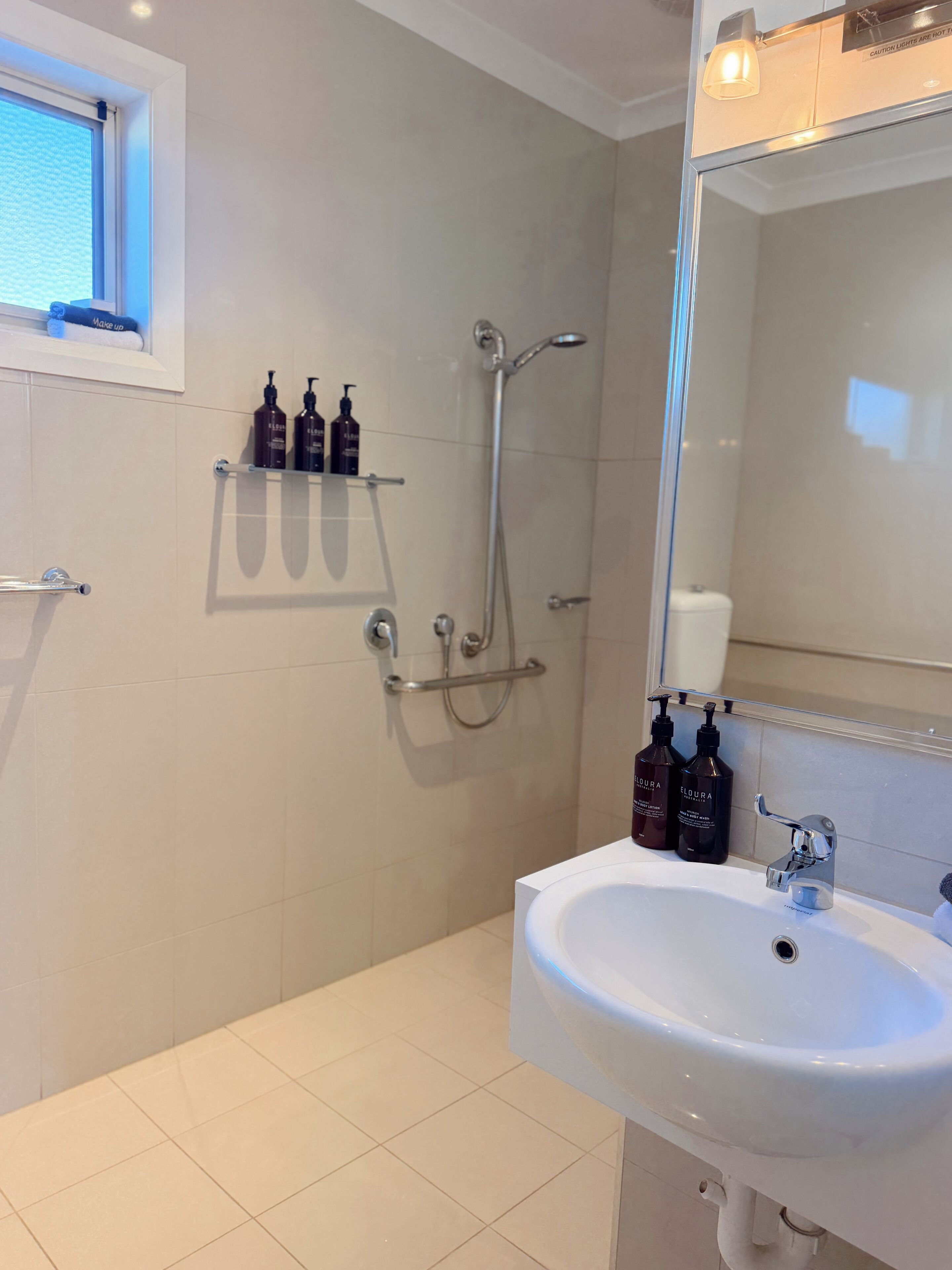 Un baño con lavamanos blanco, un espejo, ducha y artículos de aseo en un estante.