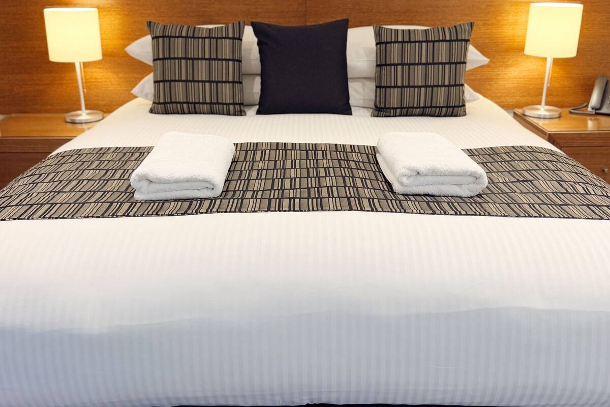 A neatly made bed with a striped bedspread, two pillows, and two folded towels.