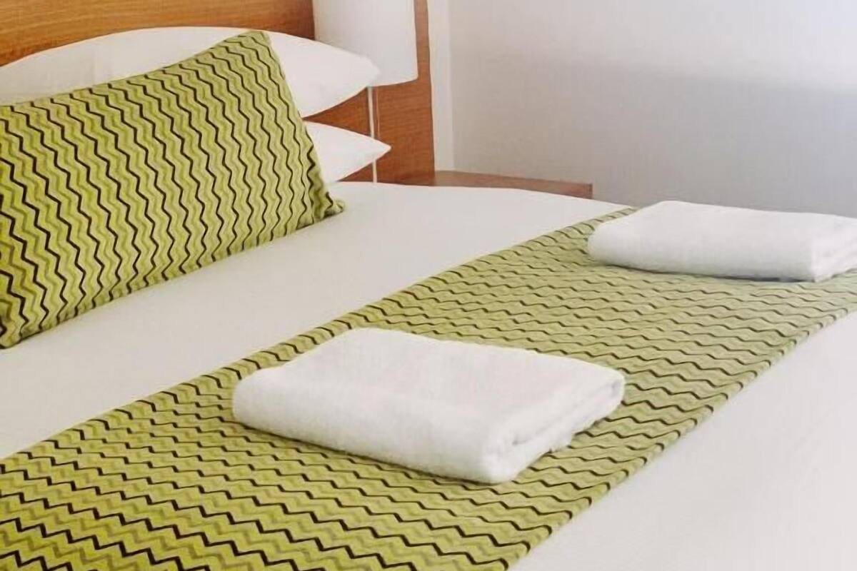 A neatly made bed with green and white bedding, a wooden headboard, and white pillows.