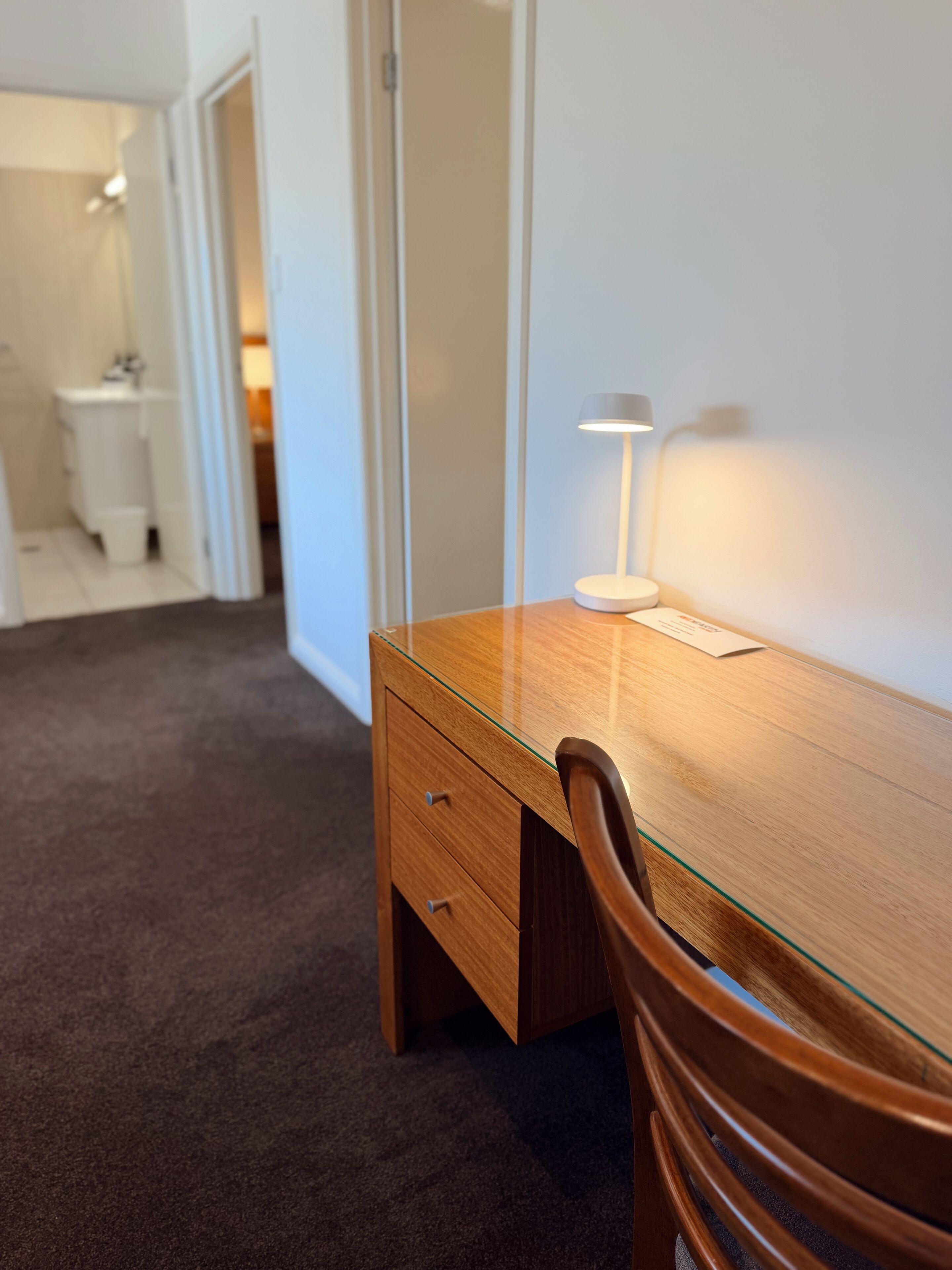 A modern office space with a wooden desk, a chair, a lamp, and a glass partition.