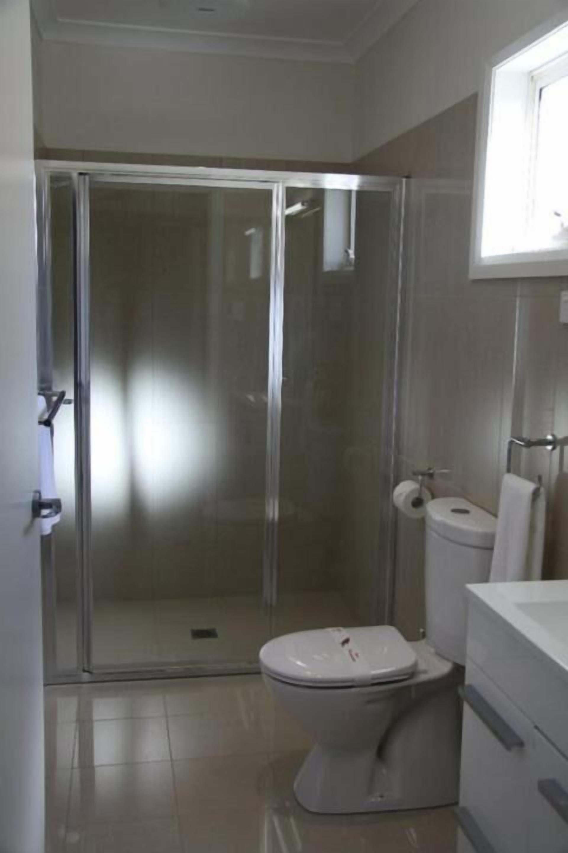 Un baño con ducha envuelta en vidrio, inodoro y lavamanos con un espejo encima.