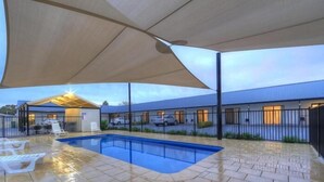 A swimming pool with a covered patio area, a building with multiple windows, and a fence surrounding the property.