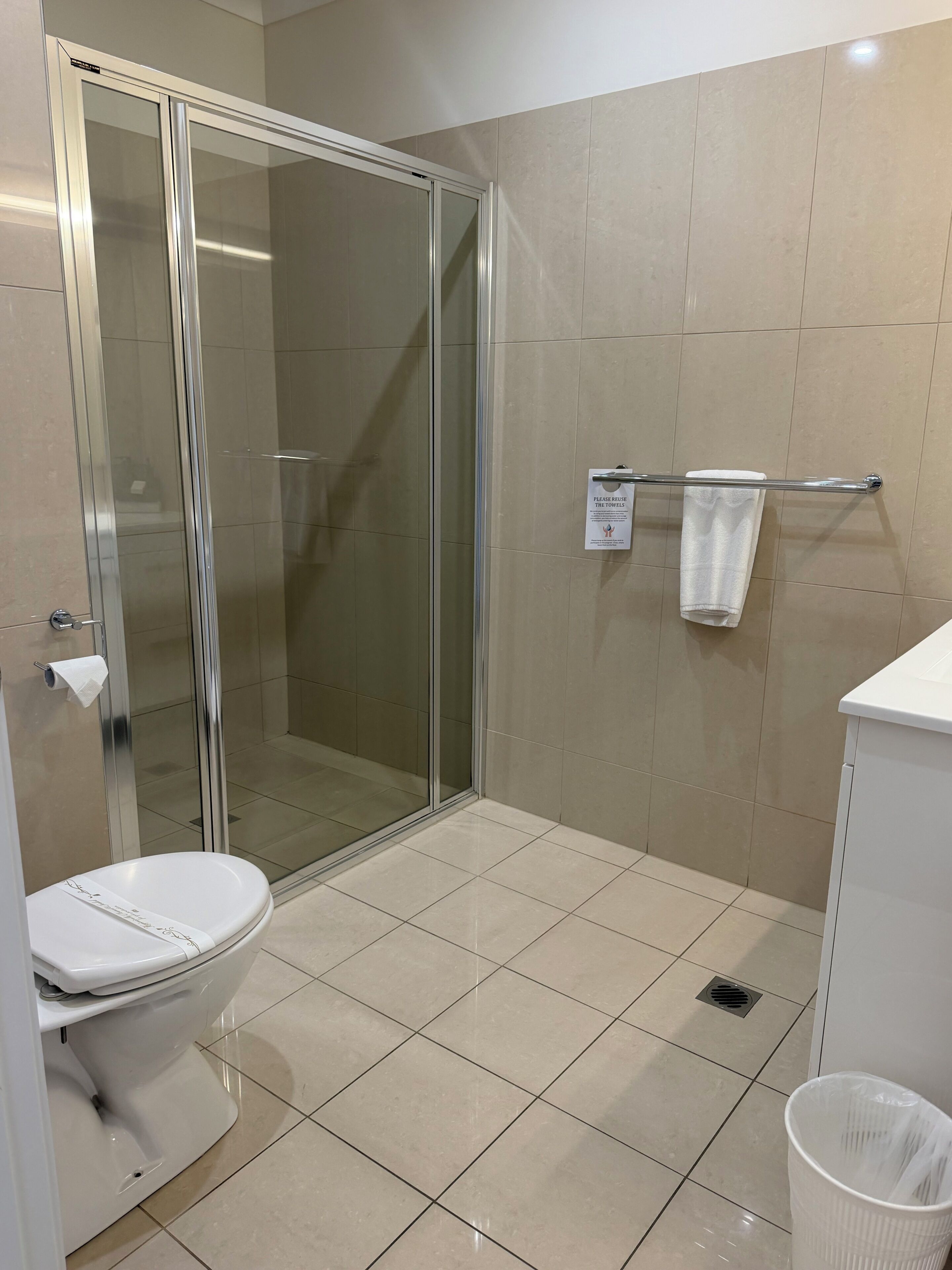 A bathroom with a glass shower enclosure, a toilet, a towel rack, and a trash bin.